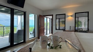 Habitación de hotel con una cama grande, una bandeja con dos tazas, un televisor y vistas al océano.