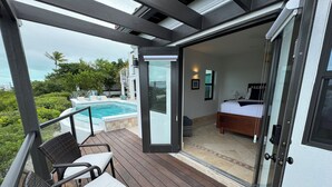 Un balcón con sillas de mimbre, una piscina y una habitación visible a través de una puerta abierta.