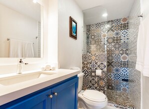 A bathroom with a white sink, blue cabinets, a white toilet, and a shower with patterned tiles. - Beach Condo on the Marina, Fully Renovated (Cabo San Lucas)