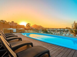 A pool area with lounge chairs, a clear view of the sunset, and a distant mountain. - Beach Condo on the Marina, Fully Renovated (Cabo San Lucas)