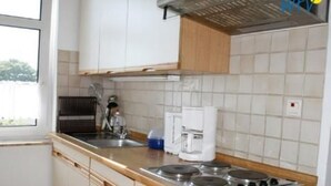 A kitchen with white cabinets, a stove, a coffee maker, and a window. - Haus Sleeboom - mit 53 qm in Ruhiger Lage Gelegen (Borkum)