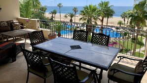 Un balcon avec une table et des chaises, donnant sur une piscine et une plage.