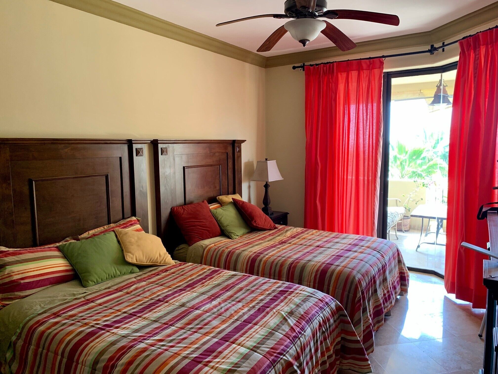 A hotel room with two beds, a ceiling fan, and a view of the outdoors through a sliding door.