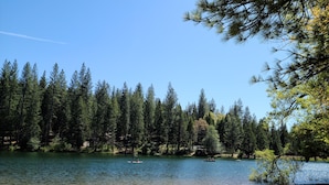 A beach with a sandy shore, a calm lake surrounded by dense trees, and a clear blue sky. - Spacious cabin with AC, private lake, hot tub, movie room (Arnold)