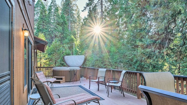 A wooden deck with outdoor furniture, a hot tub, and a view of a forest. - Spacious cabin with AC, private lake, hot tub, movie room (Arnold)