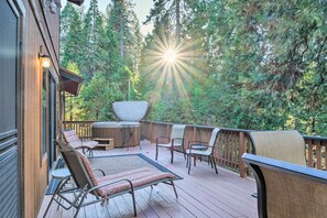 Une terrasse en bois avec des meubles d’extérieur, un jacuzzi et une vue sur une forêt.