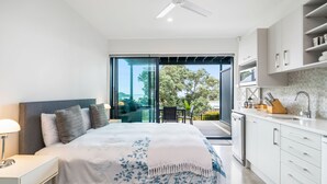 A modern bedroom with a large bed, a nightstand, a desk, and a view of the outdoors through a sliding glass door. - Bayview Corner Suite (Unit 2) - Paihia Unit (Paihia)