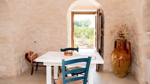 A dining area with a white table, blue chairs, a rustic vase, and a doorway leading outside. - trullo manivida (Puglia)