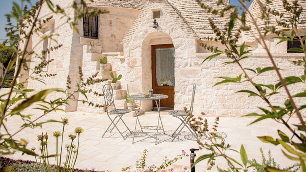 A stone building with conical roofs, a wooden door, and a small table with chairs in the foreground. - trullo manivida (Puglia)