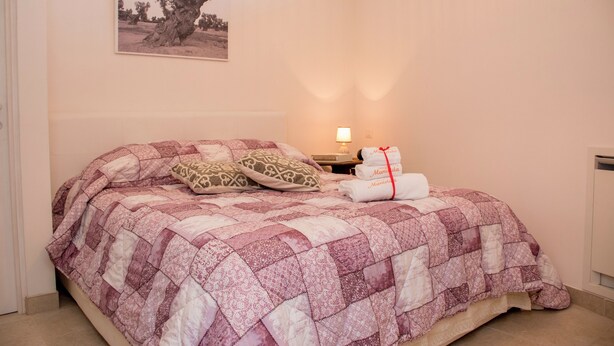 A bedroom with a bed covered in a patterned quilt, a bedside lamp, and a framed picture on the wall.