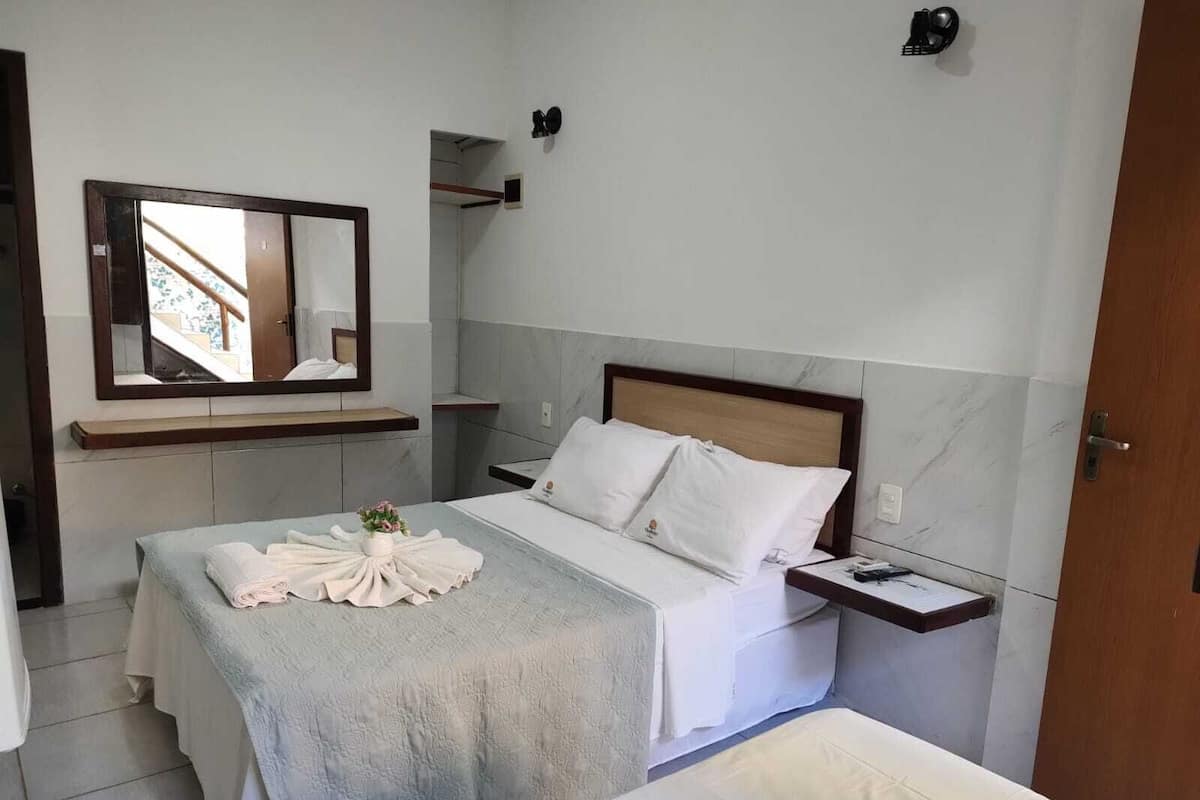 A hotel room with a bed, a bedside table, a mirror, and a bathroom visible through an open door.