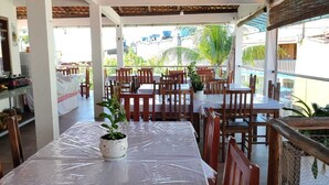 An outdoor dining area with covered tables and chairs, a grill, and potted plants. - Pousada Camburi (Cairu)