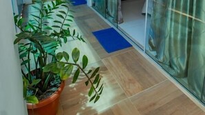 A narrow hallway with a staircase, a potted plant, and a sliding glass door leading to a room with a whiteboard and a thermostat. - Pousada Camburi (Cairu)