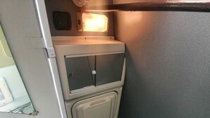 Un espacio reducido y cerrado, con un pequeño ventanal, una fuente de luz sobre un panel de control y un compartimento de almacenamiento debajo.