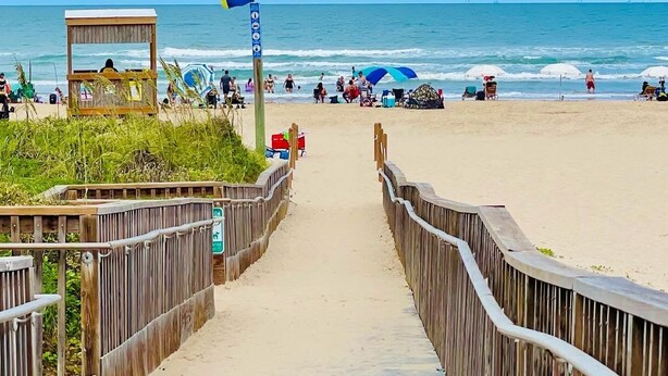 A wooden boardwalk leading to a beach with a lifeguard tower, beach umbrellas, and people enjoying the shore. - 🏖️BEACHSIDE🏖️ 2/2 Condo In The Heartbeat of SPI!! (South Padre Island)