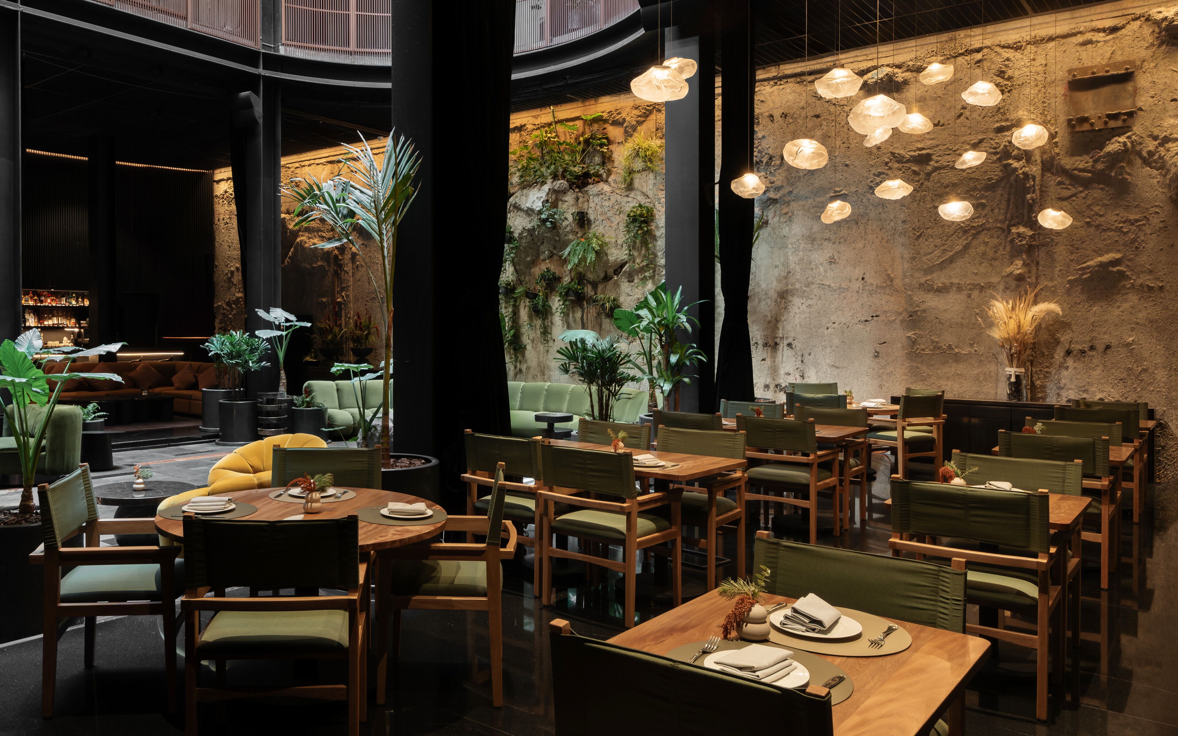 Un restaurante con mesas y sillas redondas, una zona de bar y una pared con superficie texturizada.