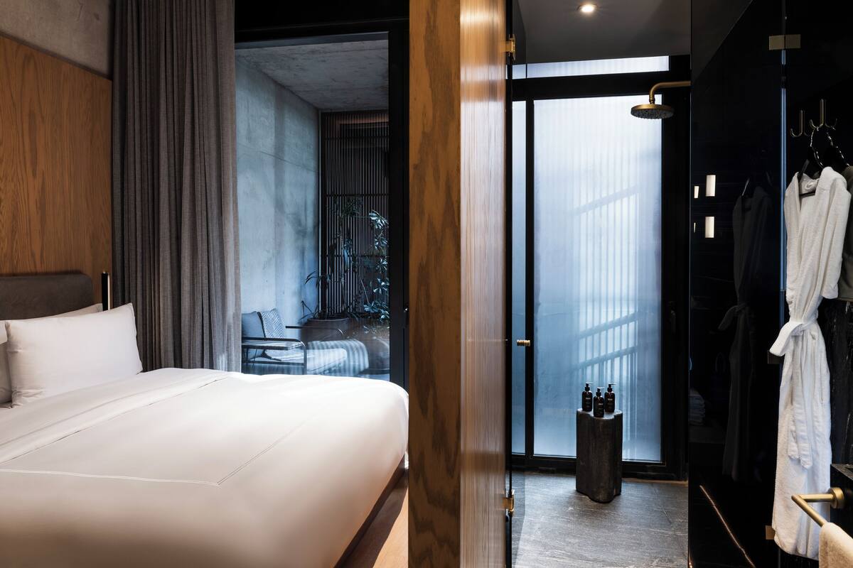 A modern hotel room with a large bed, a bathroom with a glass door, and a seating area with a view.