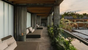 A modern outdoor seating area with a concrete floor, cushioned benches, and a view of a garden with plants and a water feature. - Volga, Member of Preferred Hotels & Resorts (Mexico City)