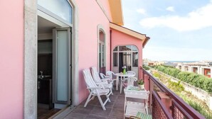 A balcony with white chairs and a table, a door leading to a kitchen, and a view of buildings and greenery. - Sea's House Moledo (Moledo)