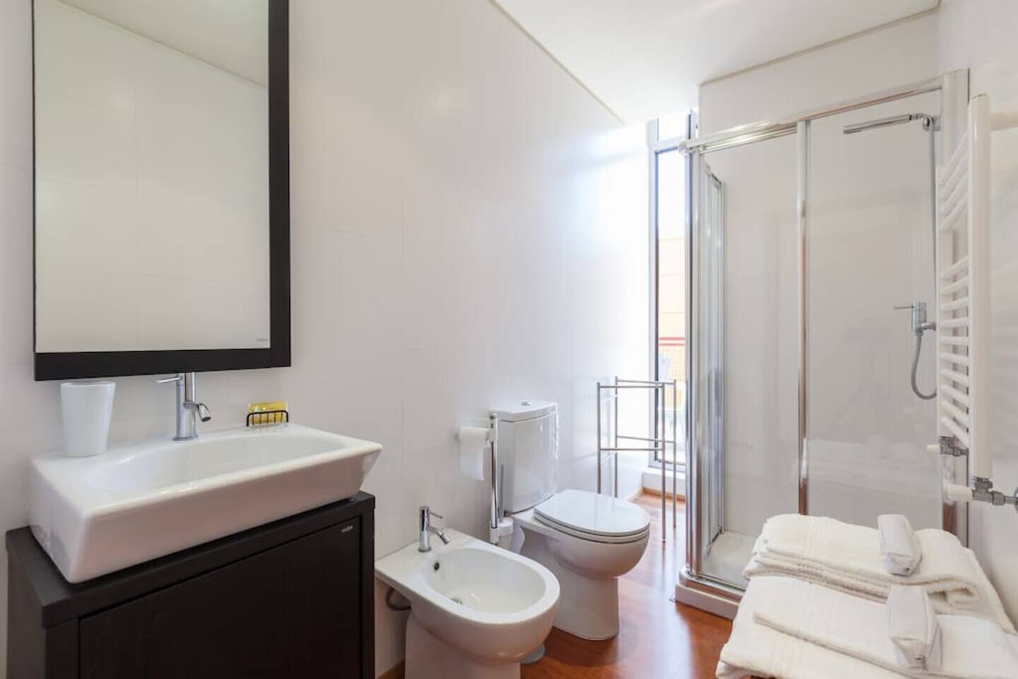 A modern bathroom with a large mirror, a sink, a bidet, a toilet, and a shower area.