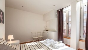 A hotel room with a bed, a desk with a lamp, two chairs, a radiator, and a window with curtains. - Sea's House Moledo (Moledo)