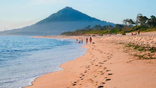 A beach with a mountain in the background, sandy shore, and people walking. - Sea's House Moledo (Moledo)