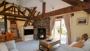 Una sala de estar acogedora con chimenea de piedra, vigas de madera, televisor y sofá.