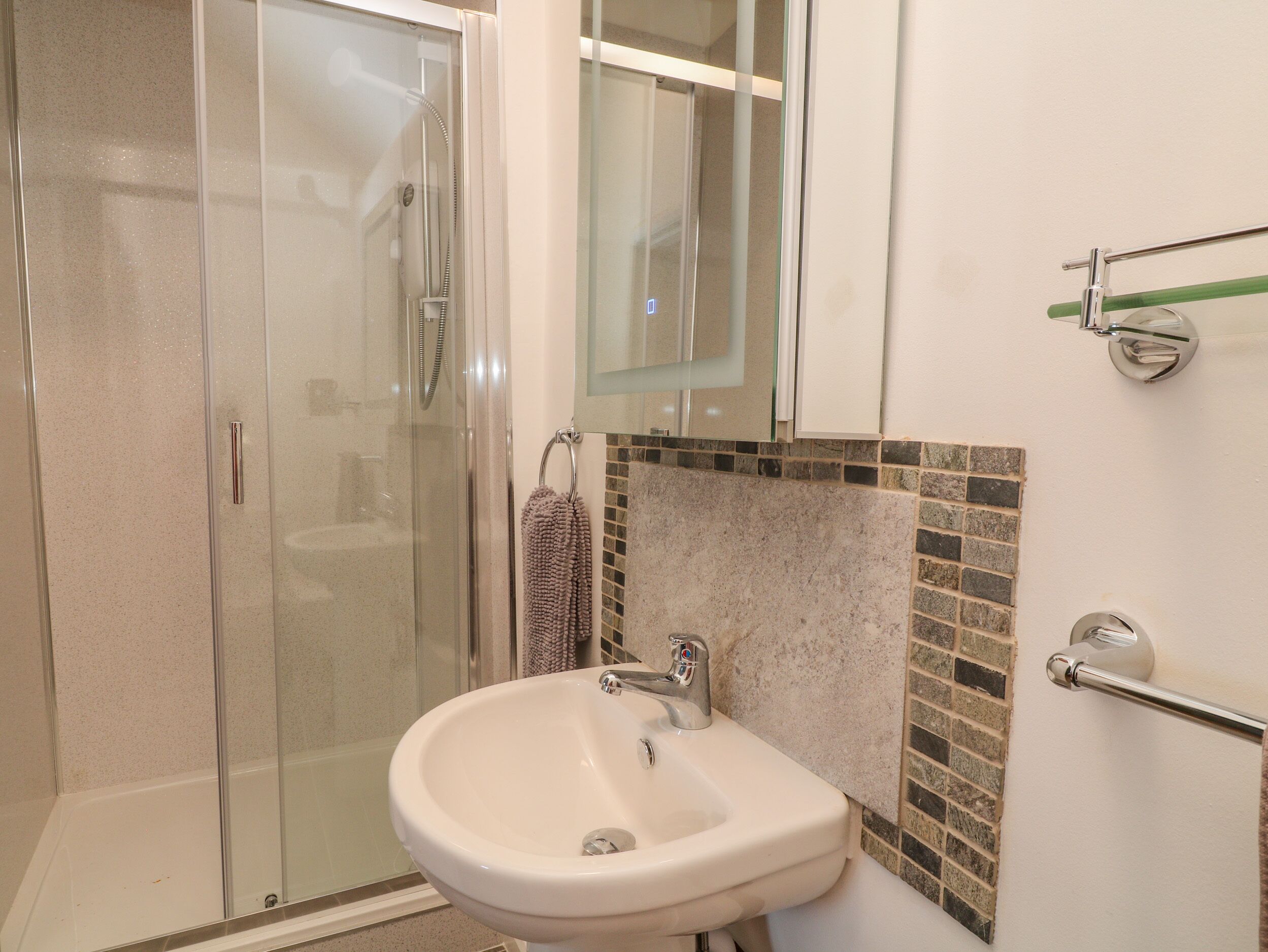 Un baño con cabina de ducha de vidrio, un lavamanos con grifo cromado y un salpicadero azulejado.