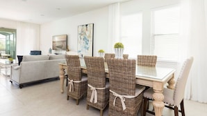 A modern dining area with wicker chairs and a glass table, a grey sofa, and a painting on the wall. - Fantabulous Disney Vacation House - Private pool, Movie Theater, Game Room (Kissimmee)