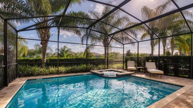 A swimming pool with a hot tub, surrounded by palm trees and a covered area with chairs. - Fantabulous Disney Vacation House - Private pool, Movie Theater, Game Room (Kissimmee)