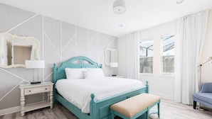 A bedroom with a bed, bedside tables, a bench, a mirror, and a window with curtains. - Fantabulous Disney Vacation House - Private pool, Movie Theater, Game Room (Kissimmee)