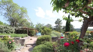 Un jardín con un sendero de piedra, un pérgola y diversas plantas y flores.