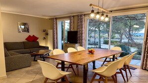 Un comedor con una mesa de madera y sillas blancas, un sofá con cojines rojos y un televisor sobre un mueble.