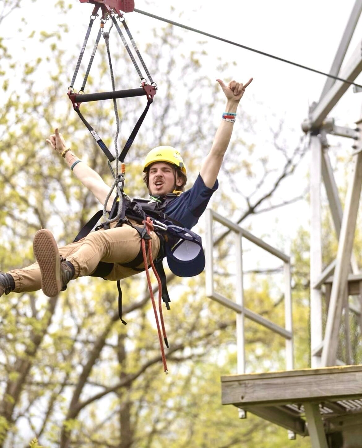 A person suspended in mid-air, secured with a harness and ropes, wearing a helmet and safety gear.