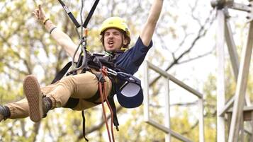 A person suspended in mid-air, secured with a harness and ropes, wearing a helmet and safety gear.
