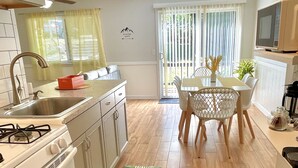 A modern kitchen with white cabinets, a gas stove, and a sink. There is a dining area with a white table and chairs.