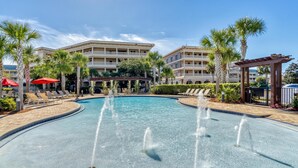 A swimming pool with water fountains, surrounded by palm trees and lounge chairs. - Newly Renovated Professionally Decorated Gulf Views! Pool & Beach Access. (Seacrest Beach)