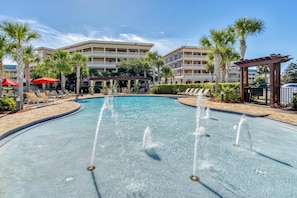 A swimming pool with water fountains, surrounded by palm trees and lounge chairs.