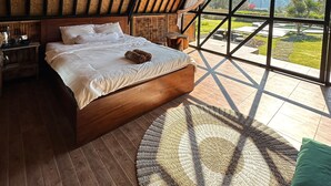 Ein Schlafzimmer mit einem großen Bett, Holzboden und Blick auf einen Garten durch große Fenster.