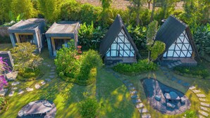 Ein Garten mit drei Häusern im traditionellen Stil, jedes mit einem Strohdach und weißen Wänden.