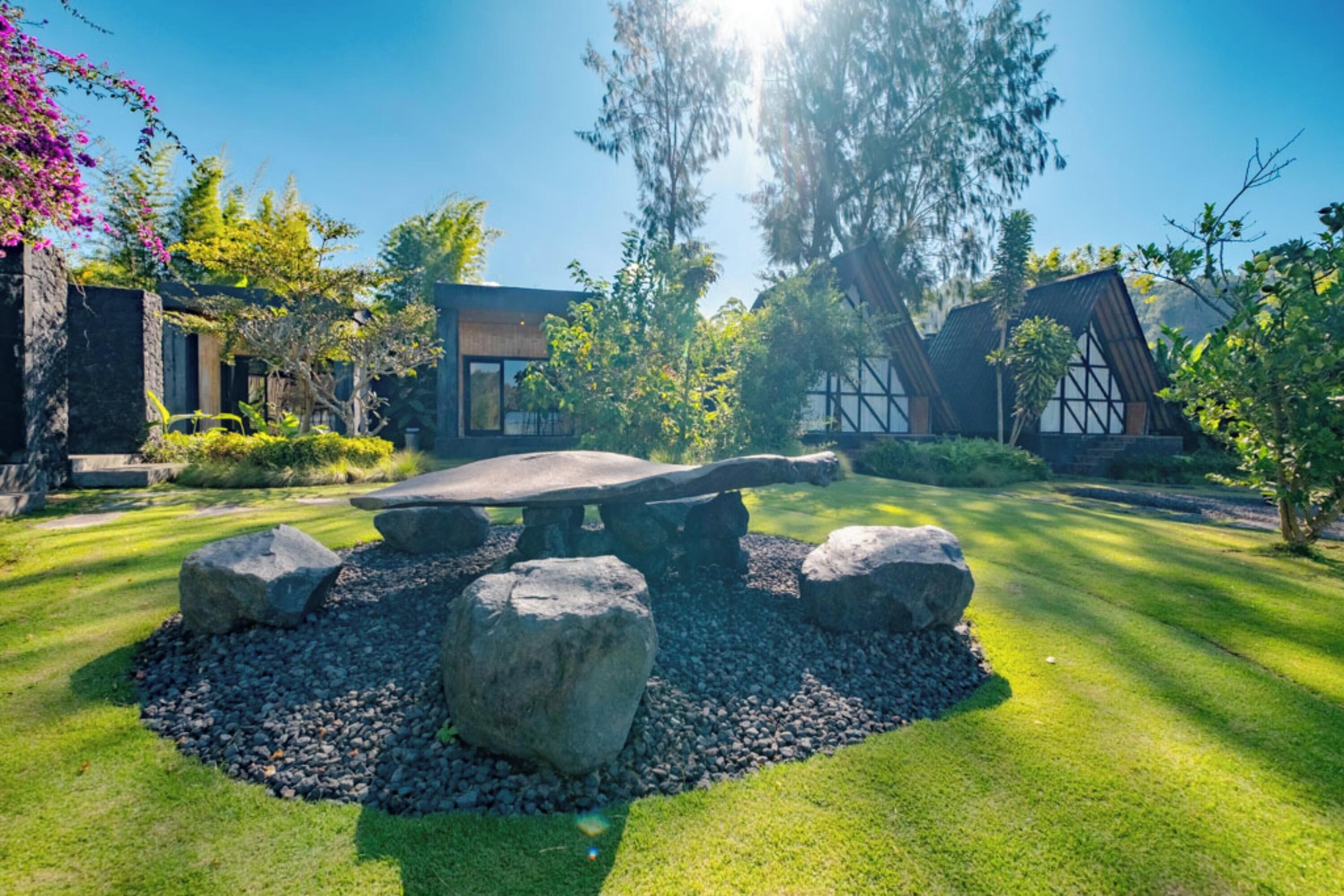 Un bâtiment moderne doté d’un banc en pierre, entouré d’un jardin bien entretenu avec de gros rochers et de la verdure.