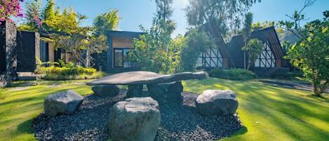 Un bâtiment moderne doté d’un banc en pierre, entouré d’un jardin bien entretenu avec de gros rochers et de la verdure.
