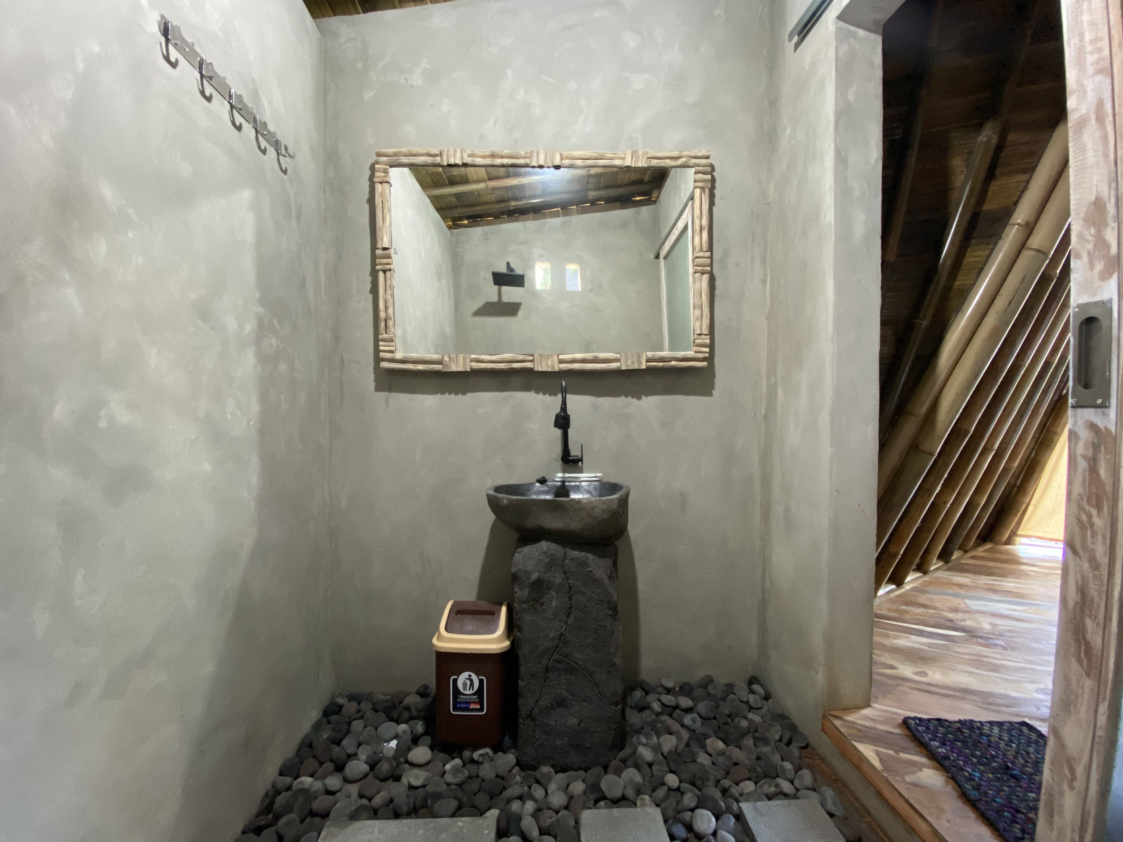 A bathroom with a stone sink, a wooden-framed mirror, and a trash bin.