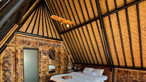 Ein gemütlicher Raum mit hohen Decken, einem großen Bett, Holzwänden und einem Strohdach.