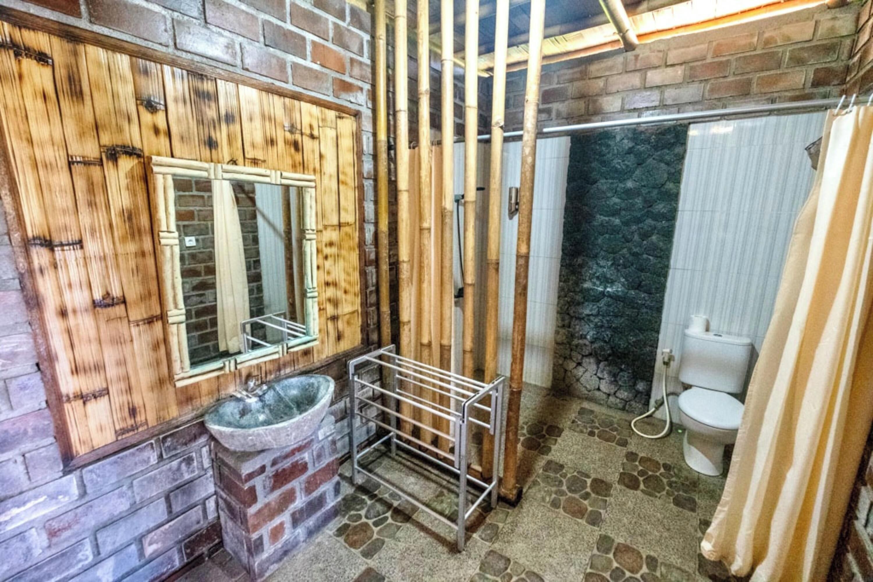 A bathroom with a stone floor, a wooden vanity, a sink, a toilet, and a shower area.