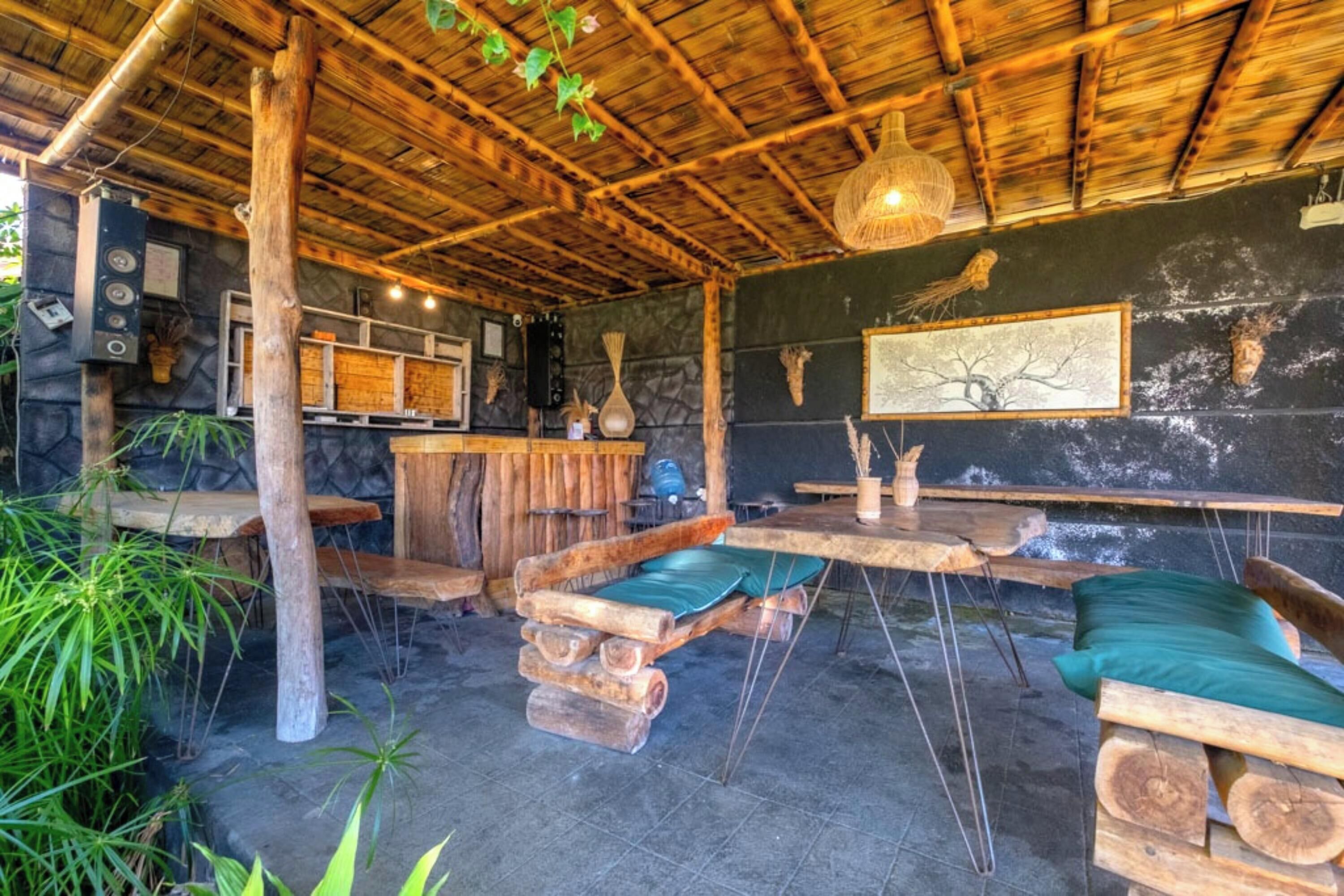 Un intérieur rustique avec un plafond en bois, des murs en pierre et un espace salon central agrémenté d’un coussin vert.
