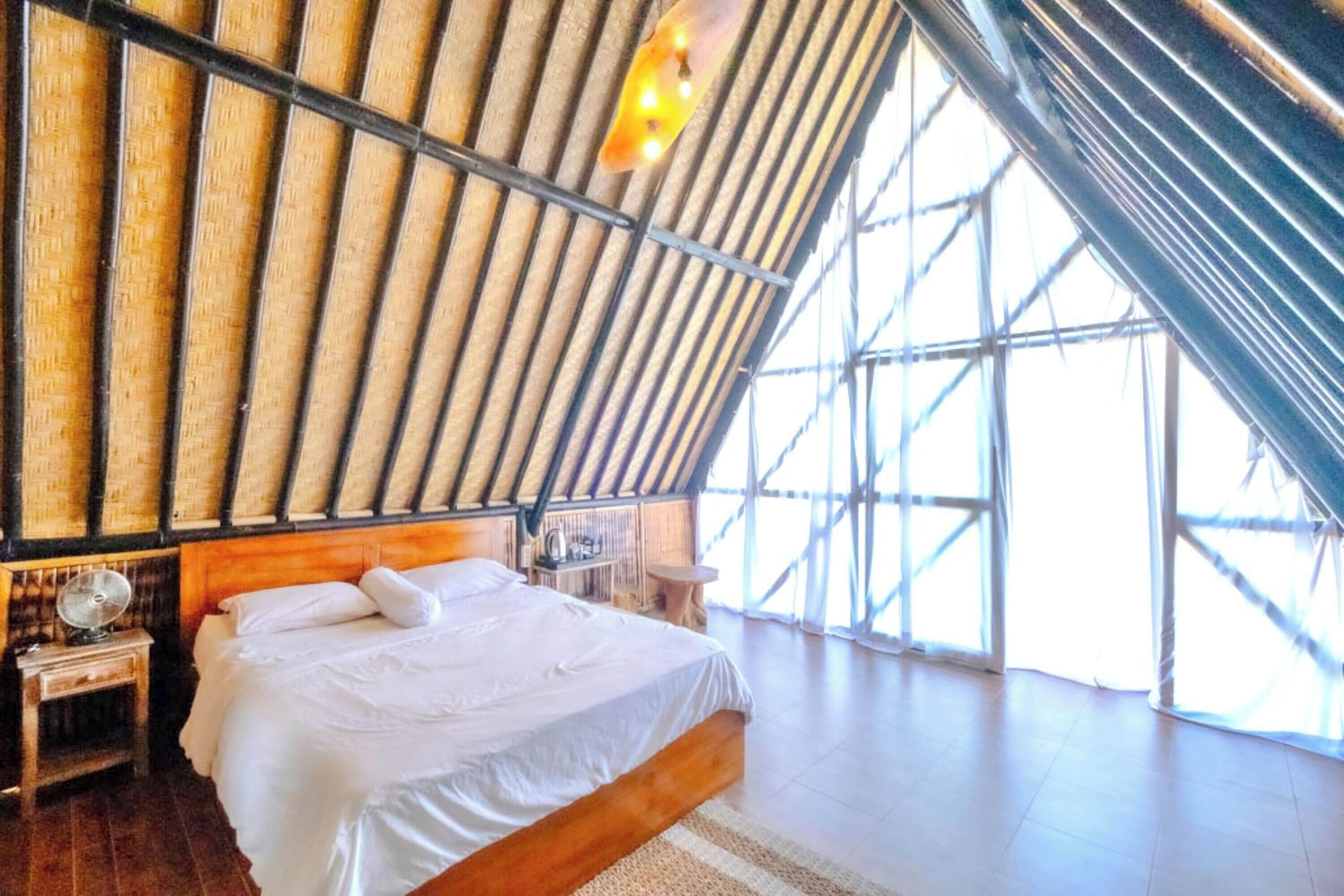 A room with a bed, wooden headboard, and a large window with a view.