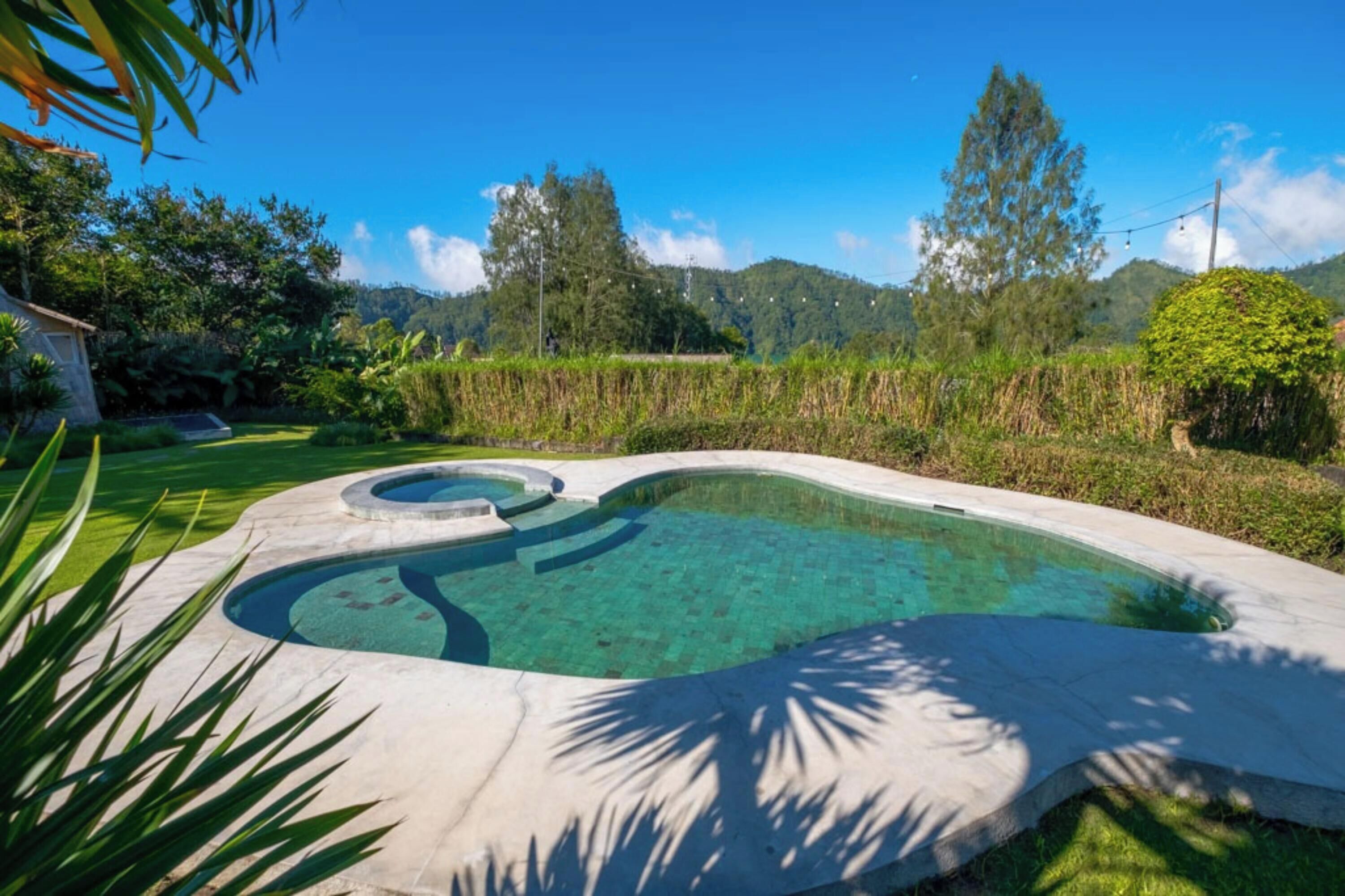 A swimming pool with a unique design, surrounded by lush greenery and hills in the background.