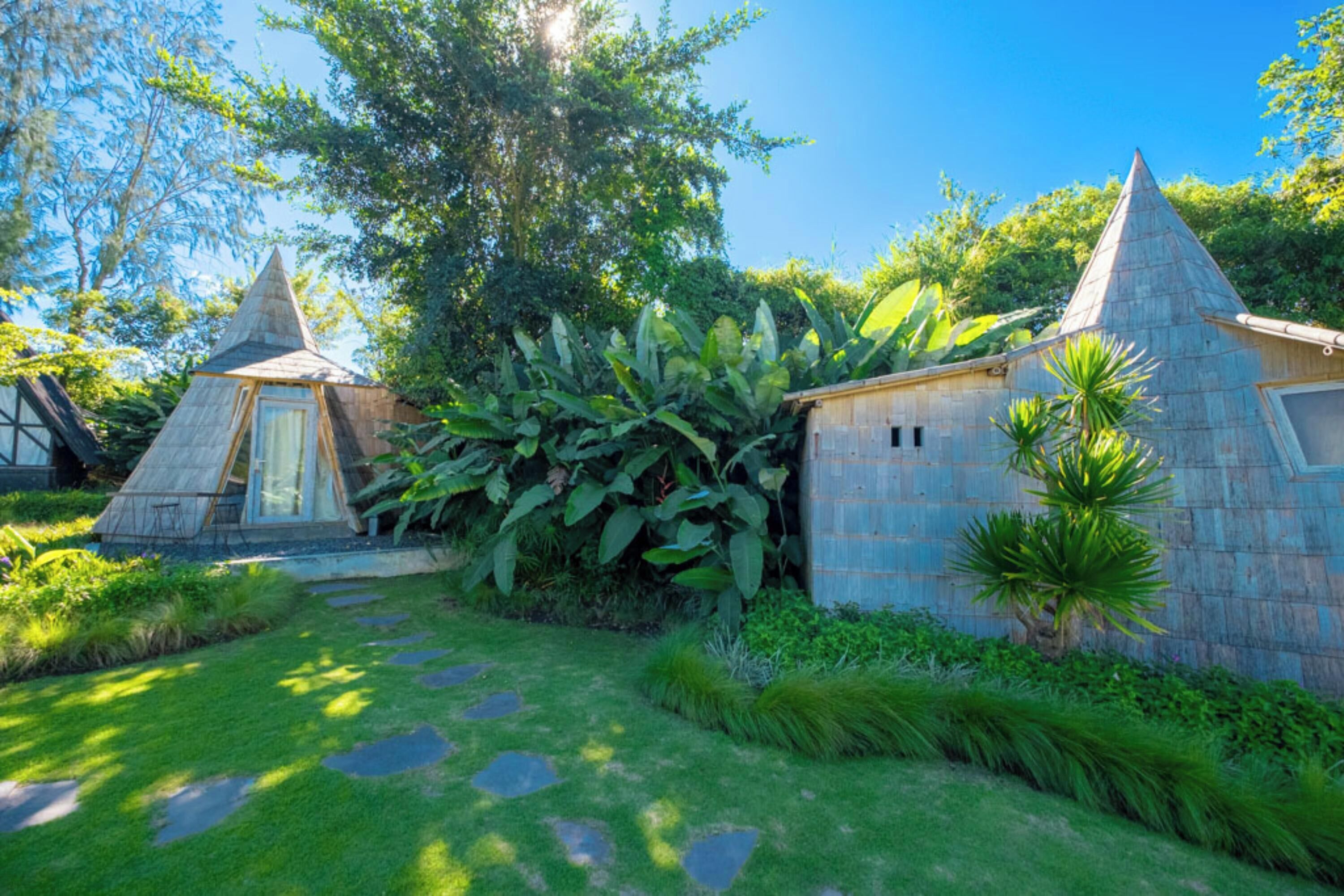 A traditional-style building with a conical roof, surrounded by lush greenery and a stone pathway.