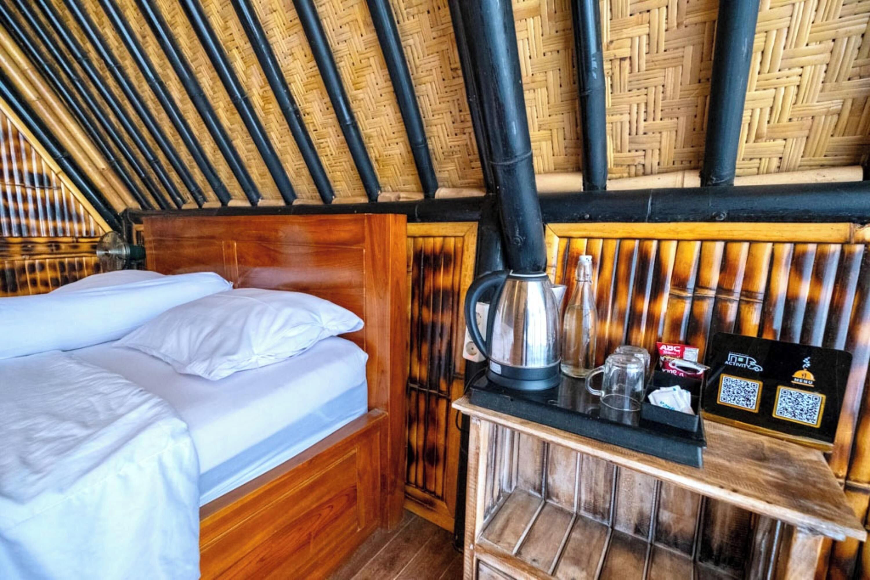A room with a bed, a wooden headboard, a bamboo ceiling, and a small table with a kettle and a cup.
